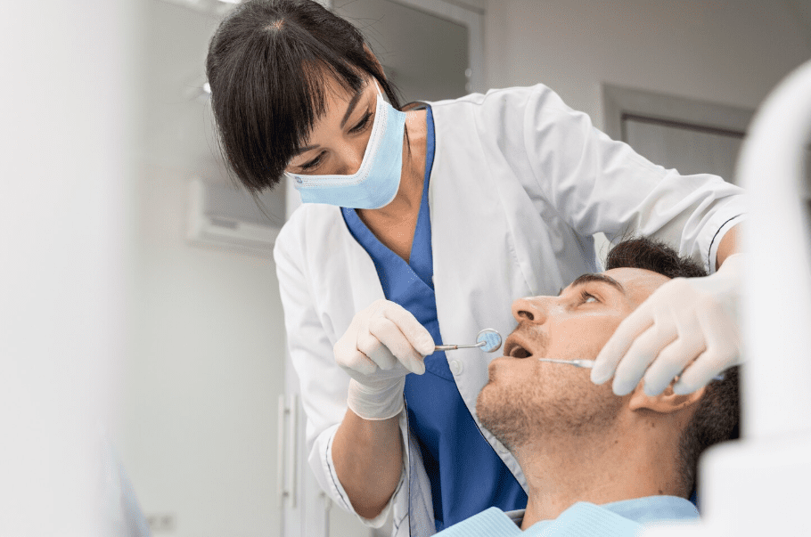 Dentist wearing a mask and gloves examines a male patient’s mouth during an oral surgery procedure in a modern dental clinic