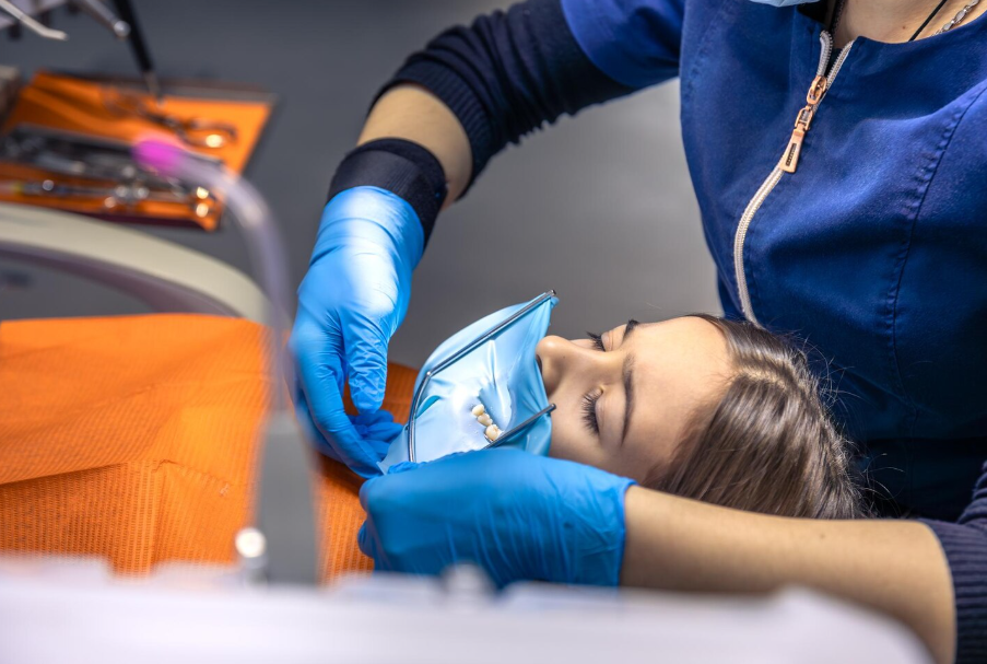 A dental professional wearing blue gloves and scrubs prepares a Emergency Dentistry Services You Can Trust in Estero dam on a patient's mouth during a procedure.