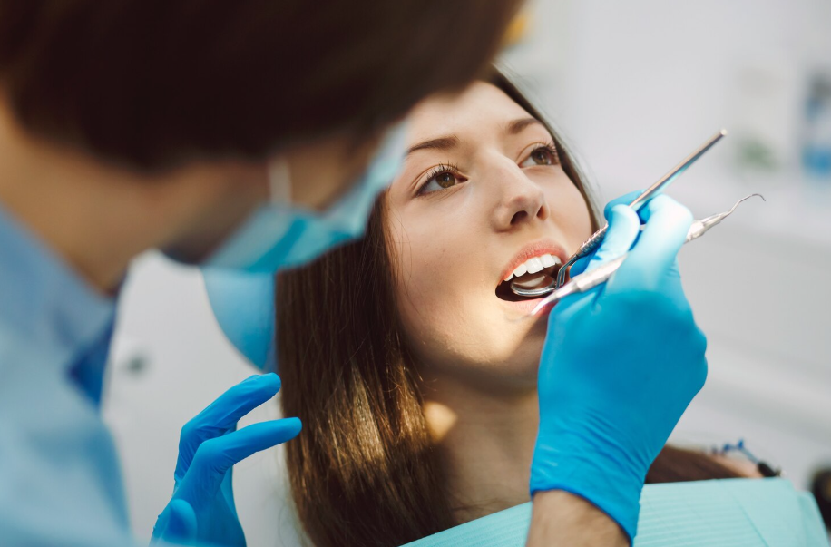 Dentist wearing blue gloves and a mask examining a female patient’s teeth during a dental checkup in a bright clinic.”